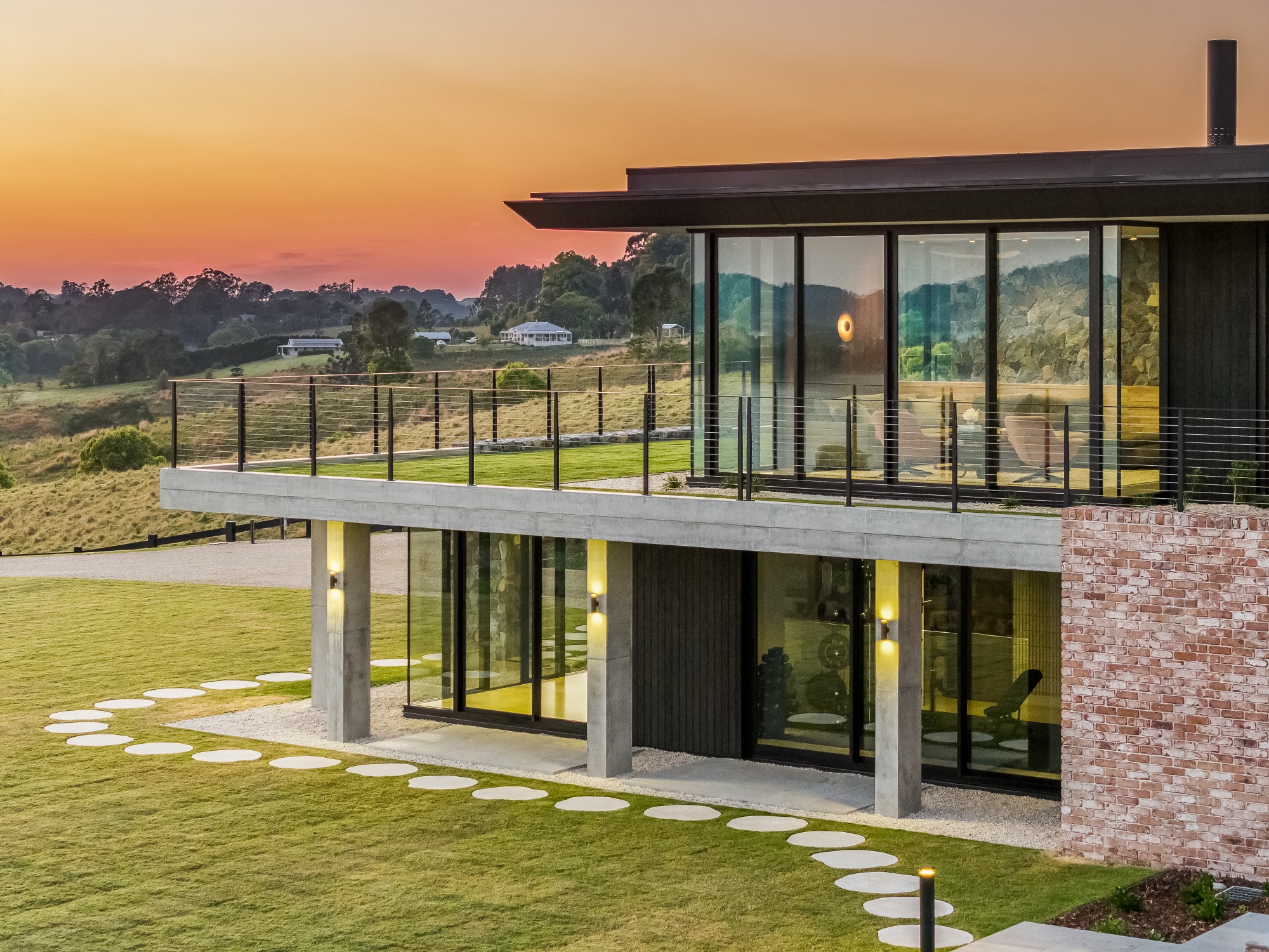 Low-angle drone showing facade, pool terrace and sunset sky