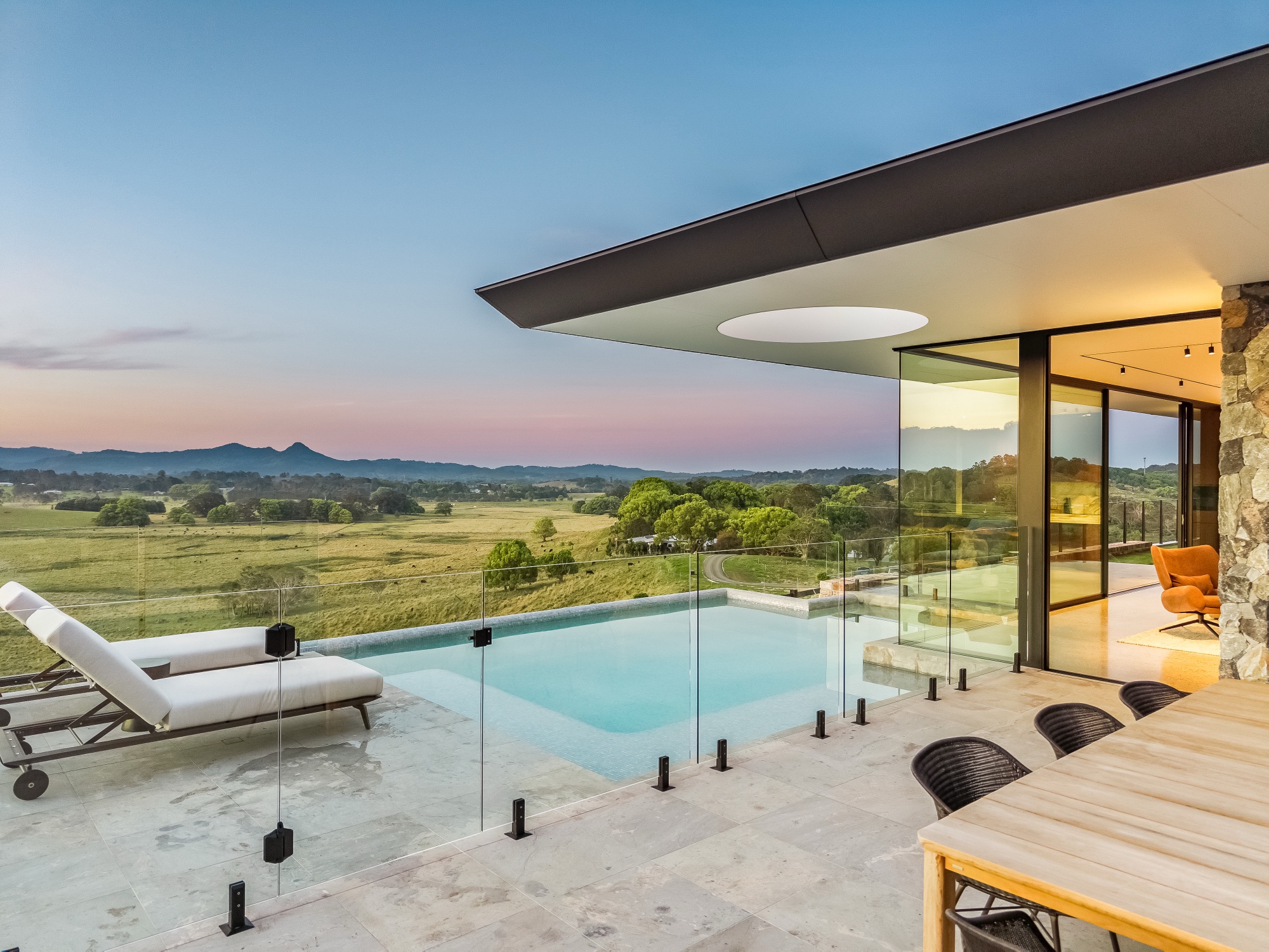 Pool and living room at twilight with warm interior glow and mountain silhouette