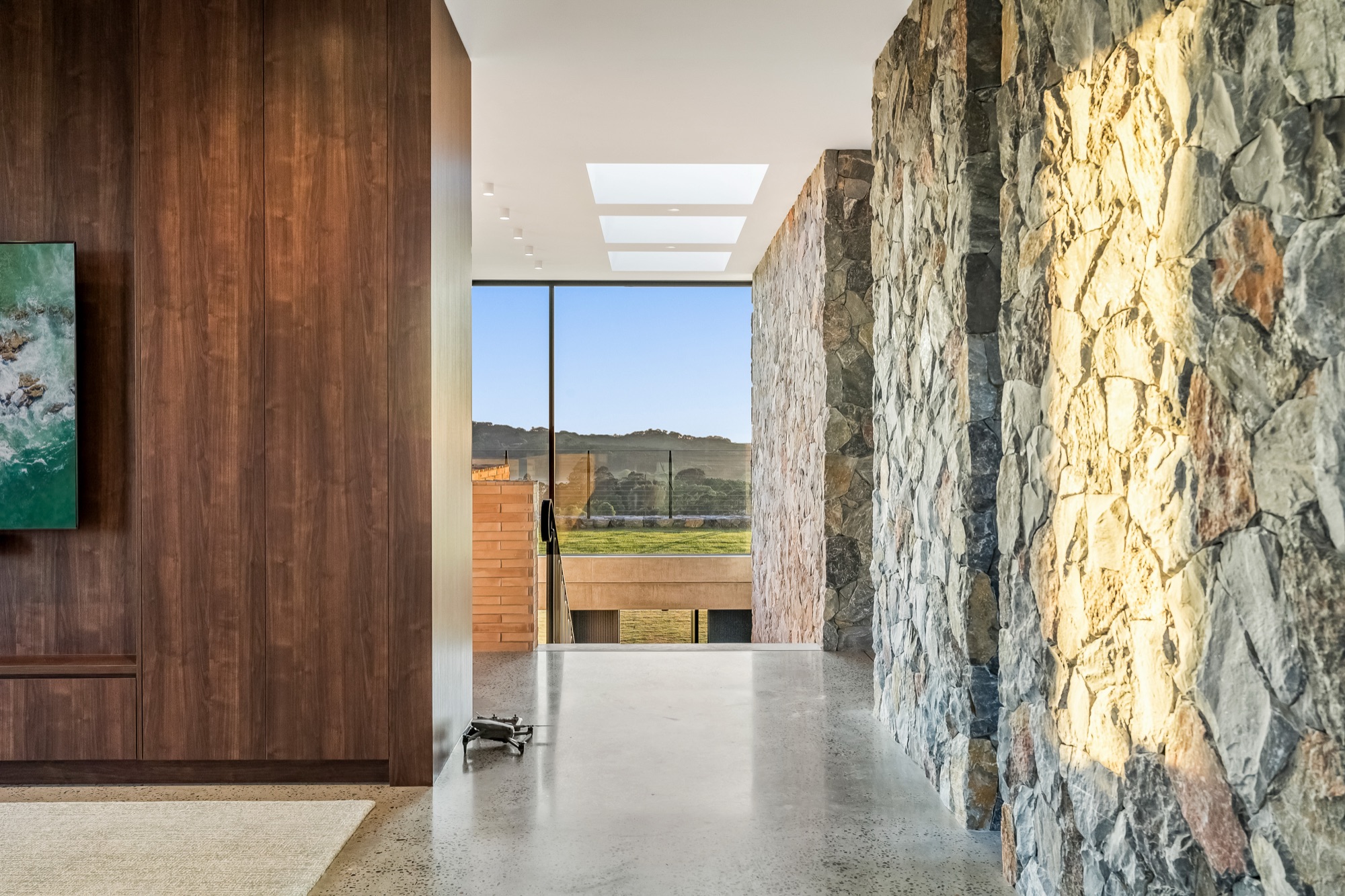 Entry hallway with walnut timber panelling, stone wall and polished concrete floors