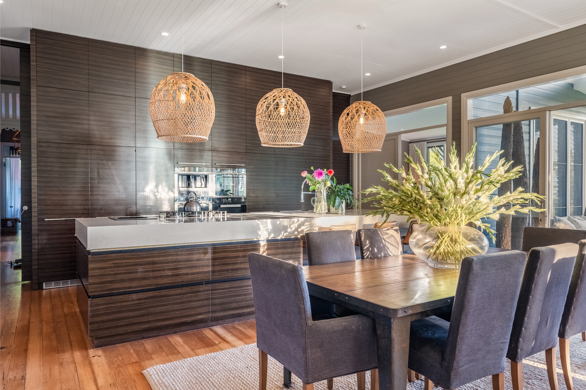 Kitchen and dining with dark timber cabinetry, stone island and rattan pendants